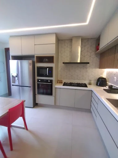 Cozinha em L com torre de forno, armários claros e bancada até a janela